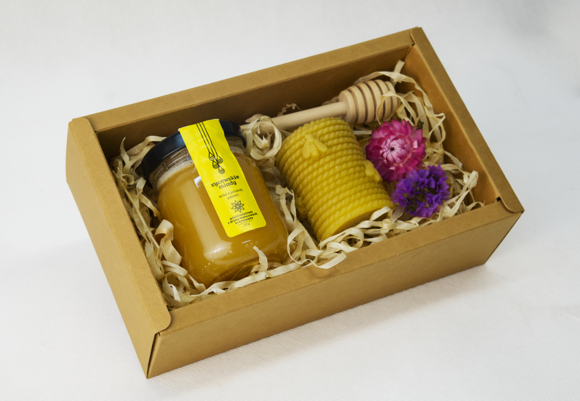 Mały słoik miodu wielokwiatowego ze świeczką z wosku pszczelego oraz drewnianym miodownikiem w kratowym boxie.