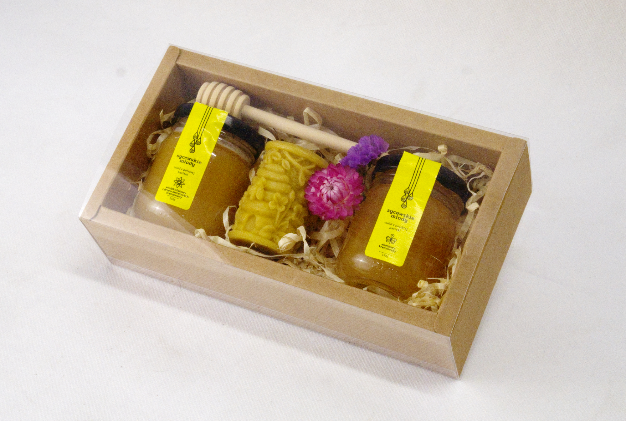 Box prezentowy z dwoma małymi słoiczkami miodu, świeczką z wosku pszczelego i drewnianym miodownikiem.
